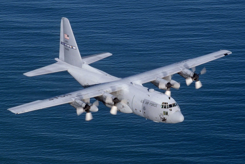 A military plane flies over blue waters.