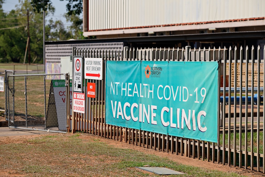A banner reading "NT Health COVID-19 Vaccine Clinic" on a fence outside a building in Katherine.