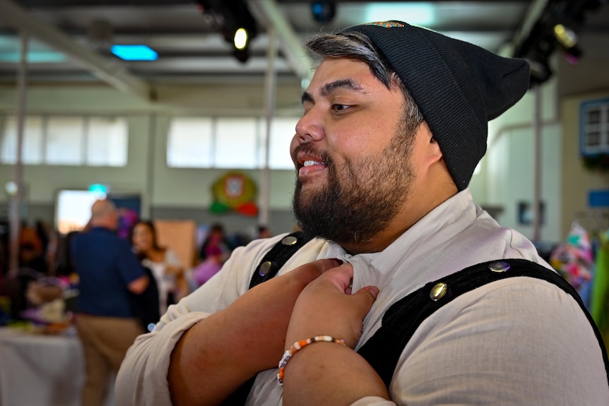 A man of adjusts his collar, he is of a large build, and wears a black beanie. 