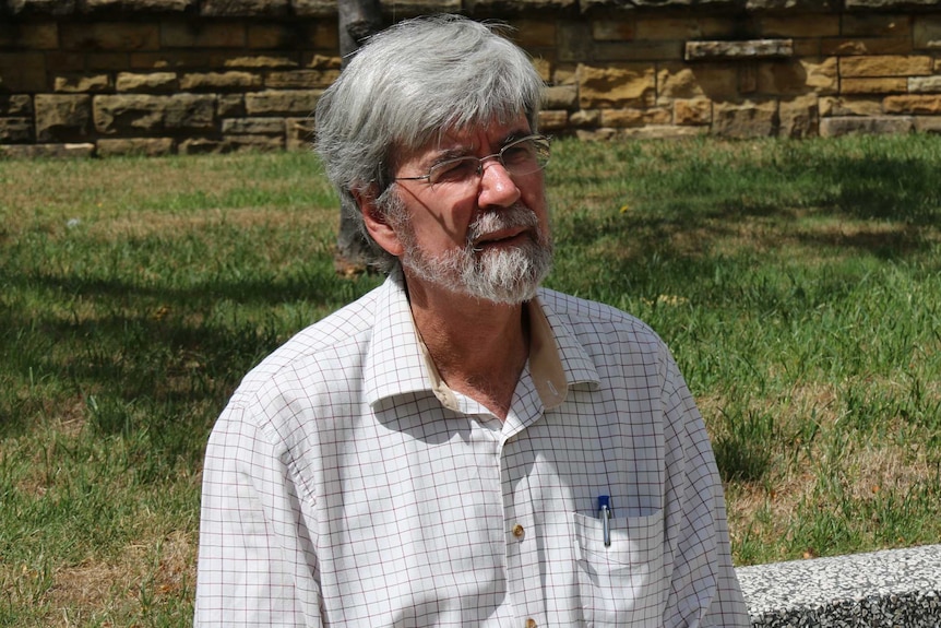 John Church sits on a granite bench with grass in the background