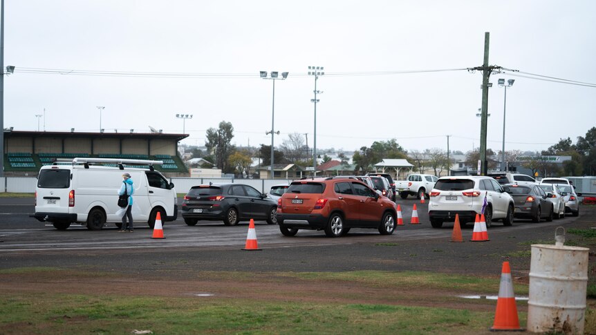 Cars lining up in a showground with a worker talking to someone in a car.