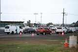 Cars lining up in a showground with a worker talking to someone in a car.