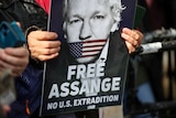 Two hands holding a poster with a picture of a man on it with his mouth covered and the words "Free Assange"