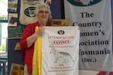 Marion Spaulding holds up the CWA tea towel with a print of a Tasmanian tiger and the words 'Let's not become extinct'.