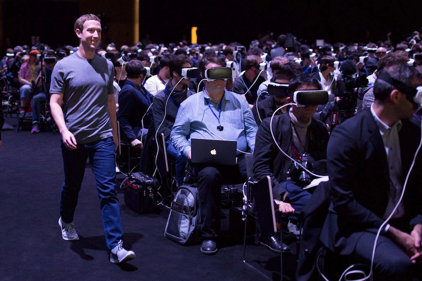 Facebook CEO Mark Zuckerberg walks past a crowd wearing VR headsets