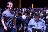 Facebook CEO Mark Zuckerberg walks past a crowd wearing VR headsets