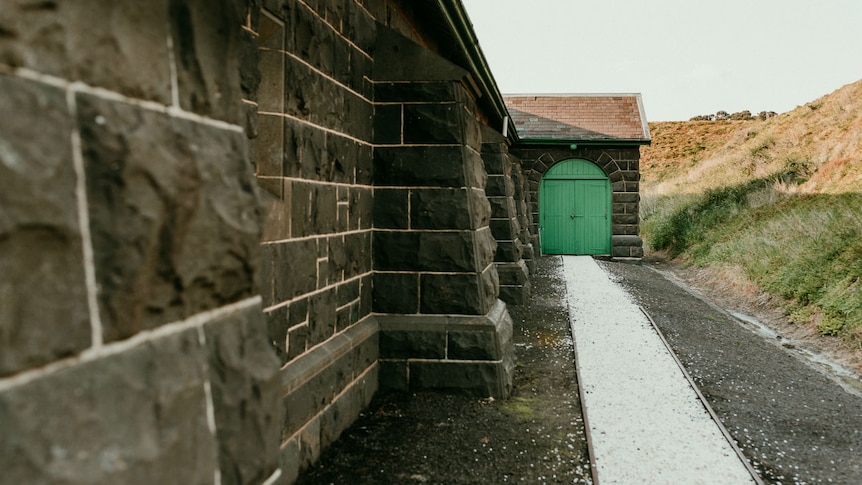 A bluestone wall leads down to a green wooden door.