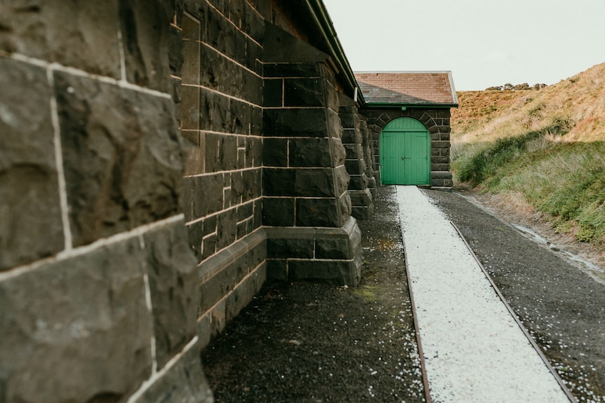 A bluestone wall leads down to a green wooden door.