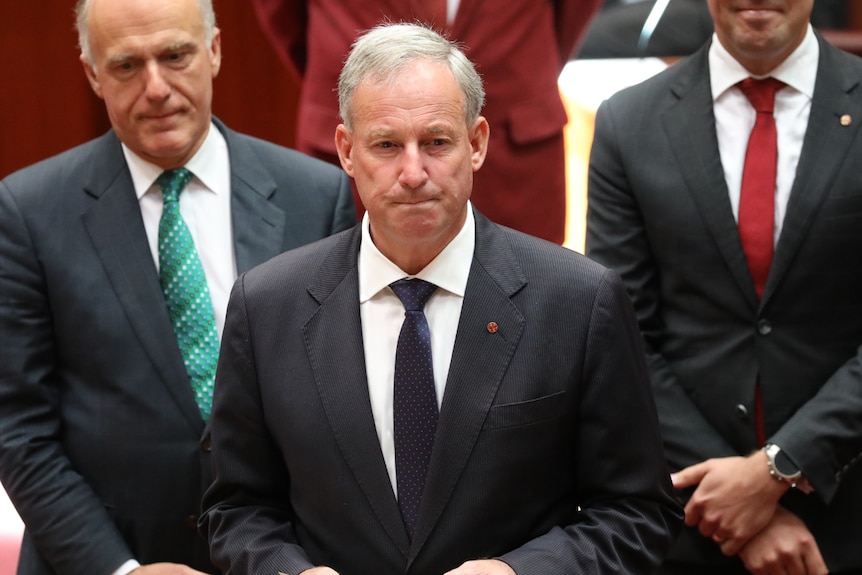 Richard Colbeck, wearing a dark suit with a red pin on his lapel, being sworn into Federal Parliament.