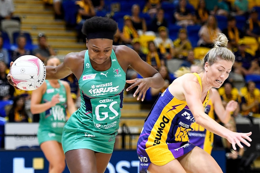 A Melbourne Vixens Super Netball player holds the ball in her right hand, with a Sunshine Coast Lightning opponent next to her.
