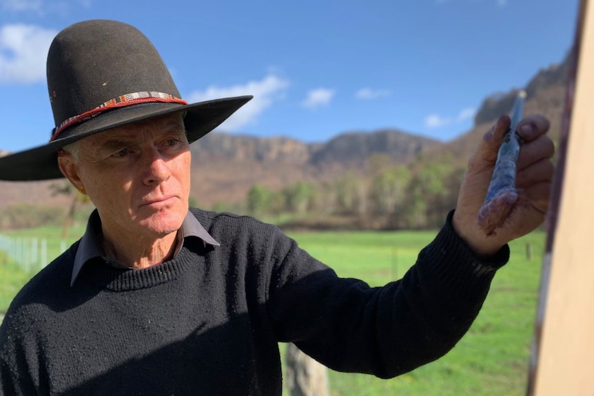 Warwick Fuller paints, wearing a wide-brimmed hat.