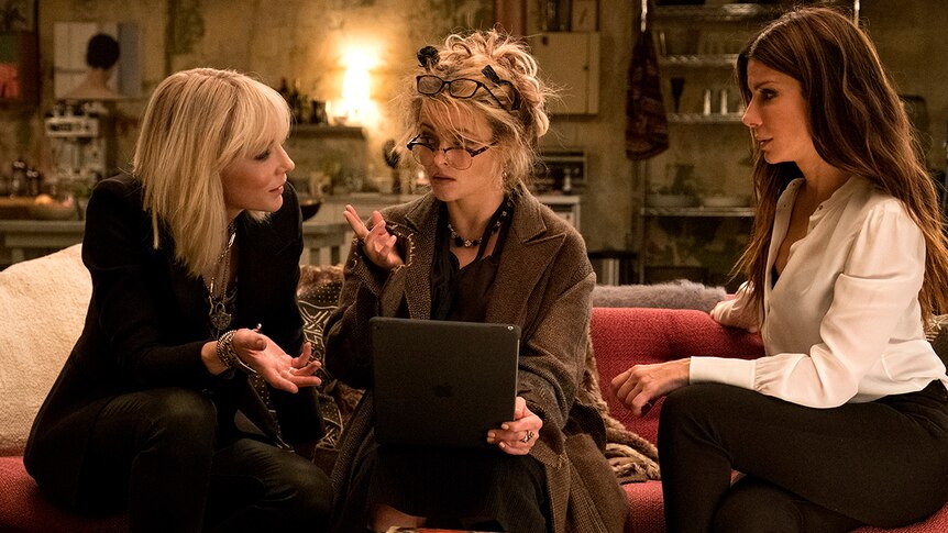 Colour photo of Cate Blanchett, Helena Bonham Carter and Sandra Bullock sitting on a living room couch in 2018 film Ocean's 8.
