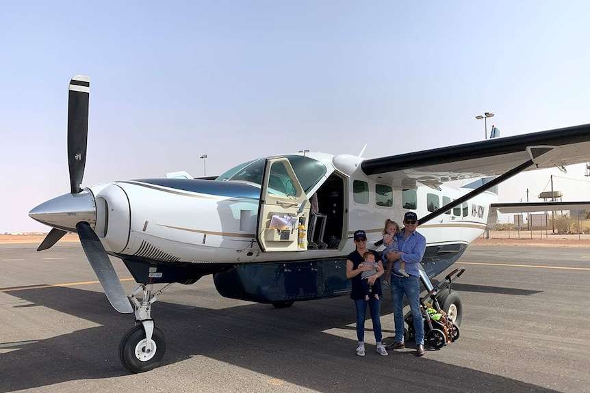 A man, woman, and two children stand outside a small propeller plane at an outback aerodrome.
