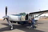 A man, woman, and two children stand outside a small propeller plane at an outback aerodrome.