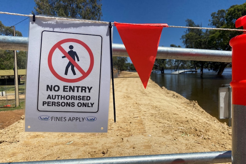A sign saying NO ENTRY and bunting on a levee next to a river