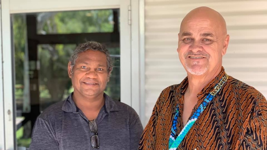 Two Aboriginal men stand smiling outside a building