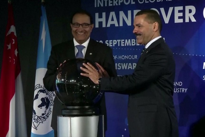 Two men place their hands on a spherical object at a media event.