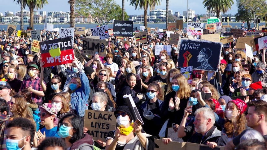 People stand in a crowd wearing masks and holding Black Lives Matter signs.