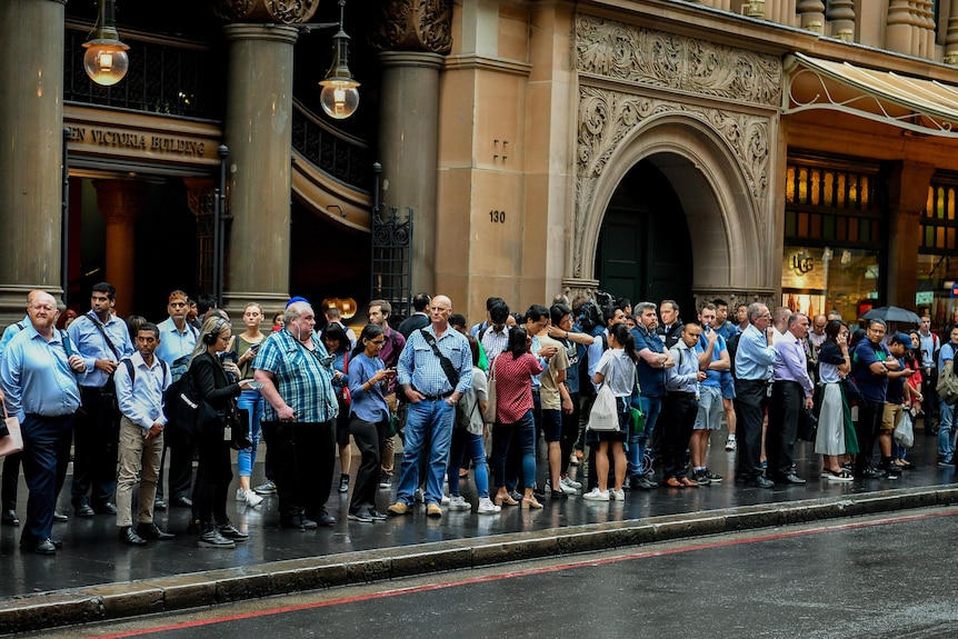 A long line of people stand on the pavement. 