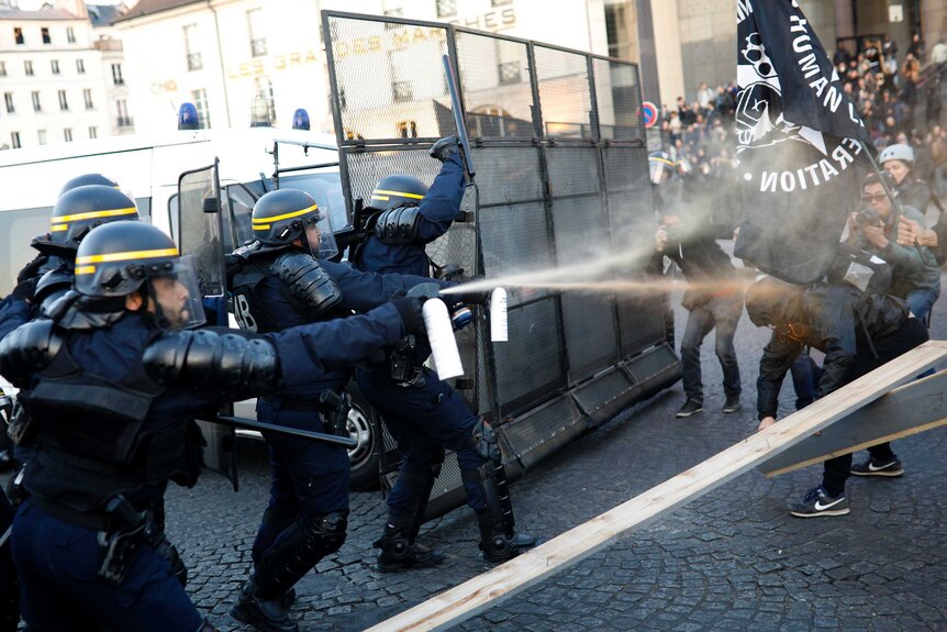 Police officers spray gas on demonstrators.