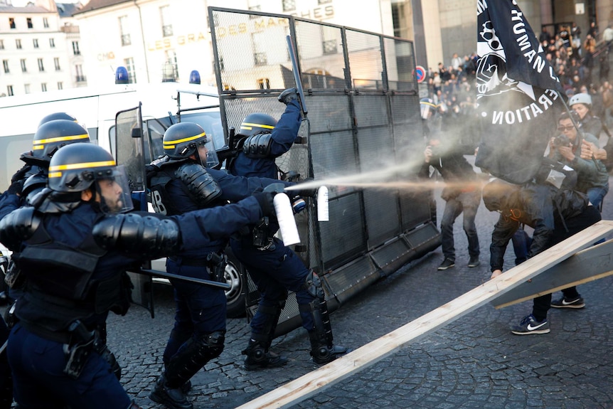 Police officers spray gas on demonstrators.