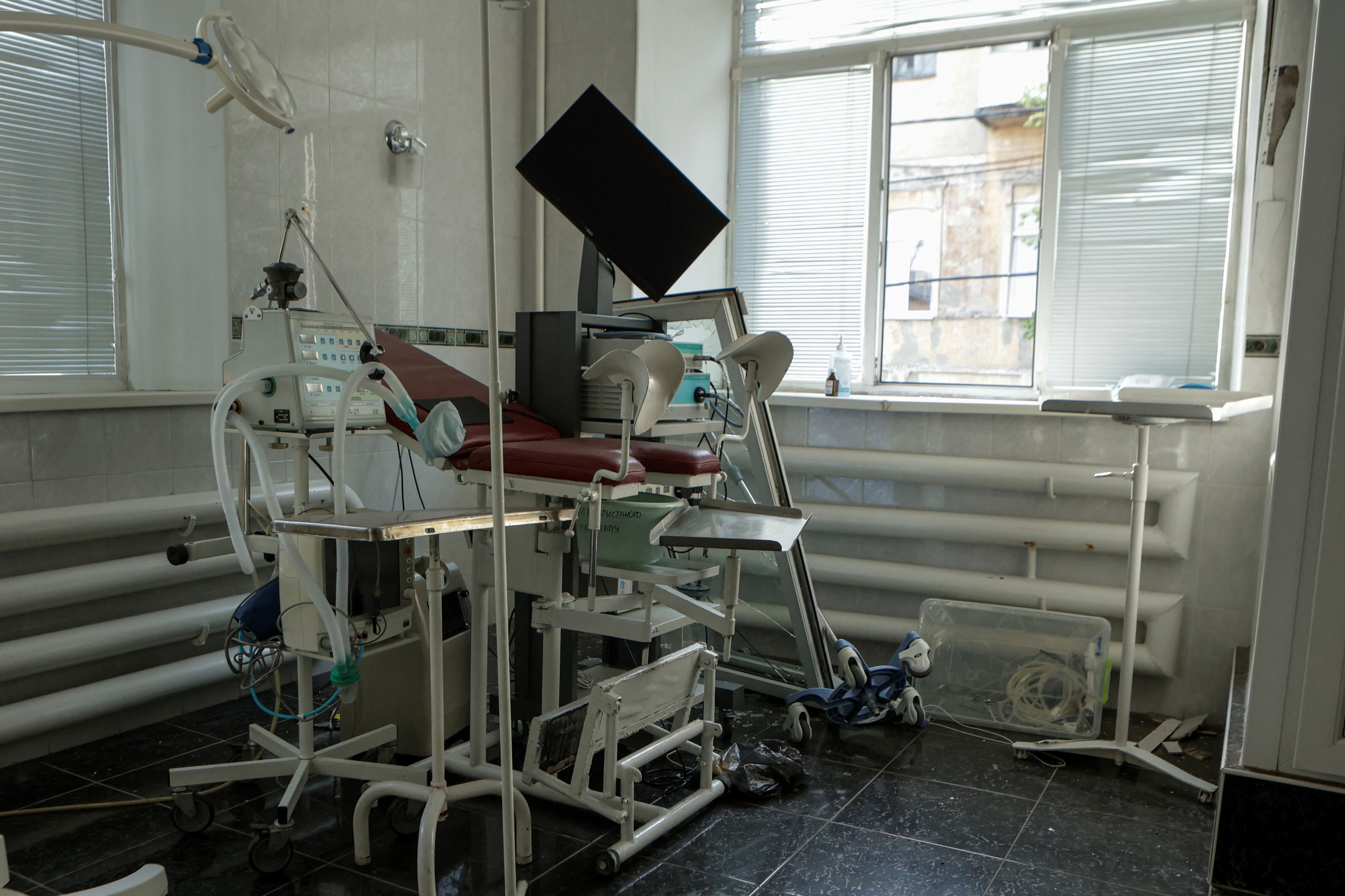 Medical equipment sits in a room damaged, with a broken window leaning against it