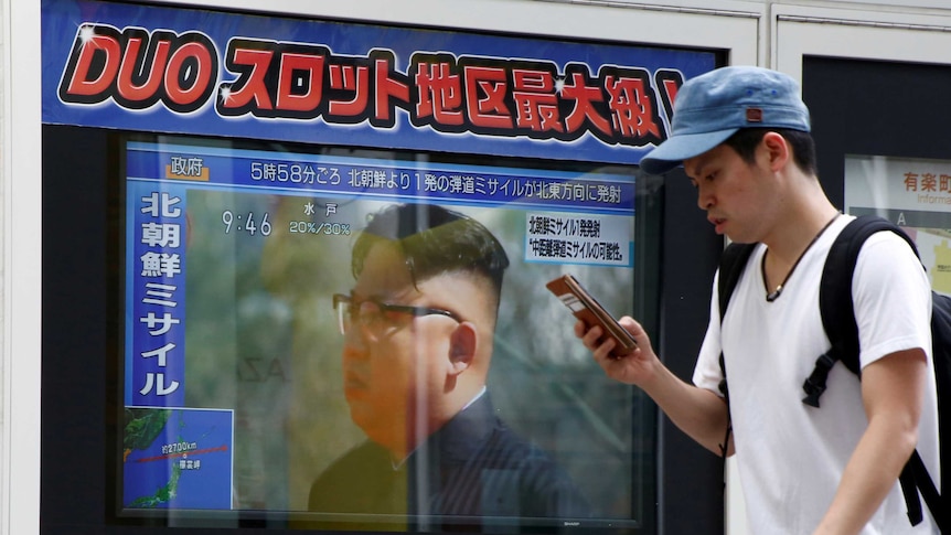 A an walks past a TV set showing North Korea's leader Kim Jong-Un in a news report about North Korea's latest missile launch.