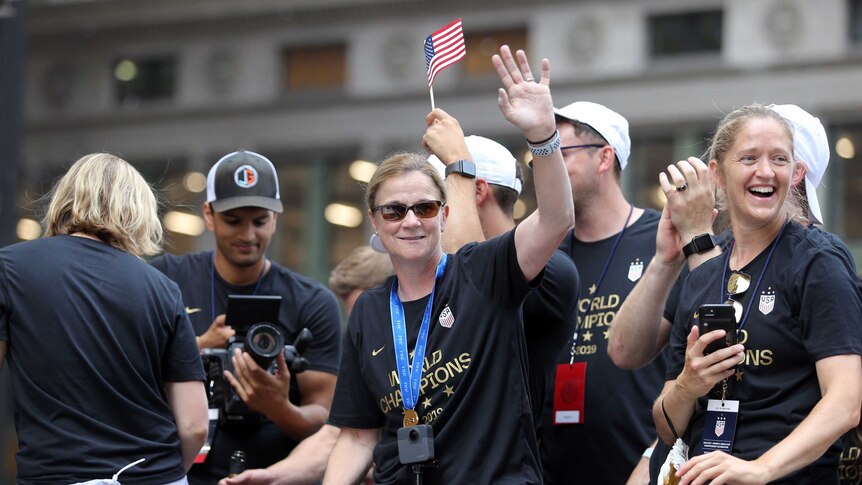 A woman stands on a float wearing sunglasses and a "World Champions" T-shirt, waving at the crowd.