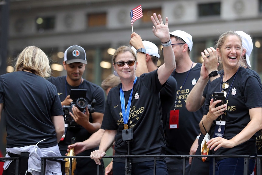 A woman stands on a float wearing sunglasses and a "World Champions" T-shirt, waving at the crowd.