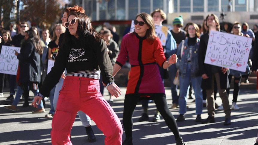 Dancers, some with signs stand in Garema Place, some wearing sunglasses.