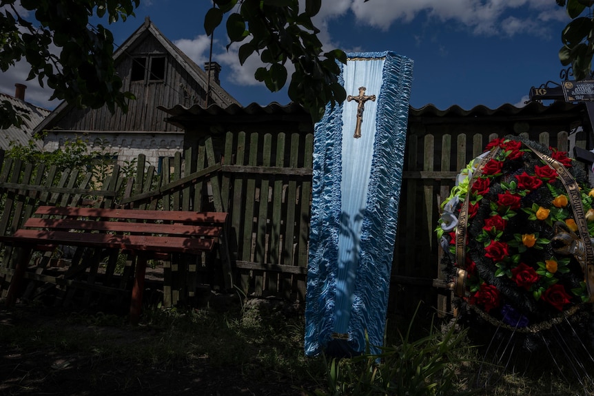 A blue coffin and a flower tribute is leaned against a damaged fence. 