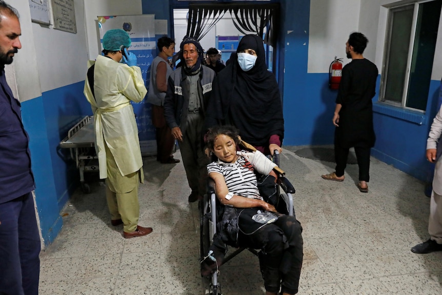 A woman pushes an injured girl in a wheelchair