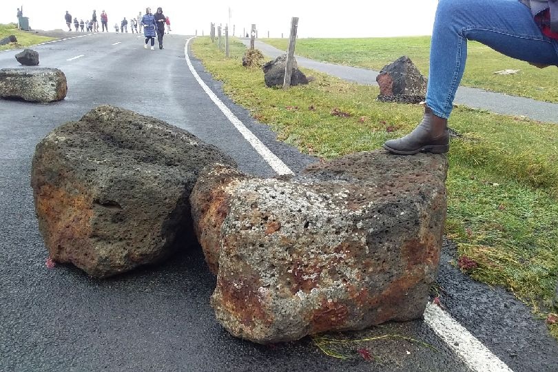 Large boulders lie across a road, people in the distance are looking at the rocks.