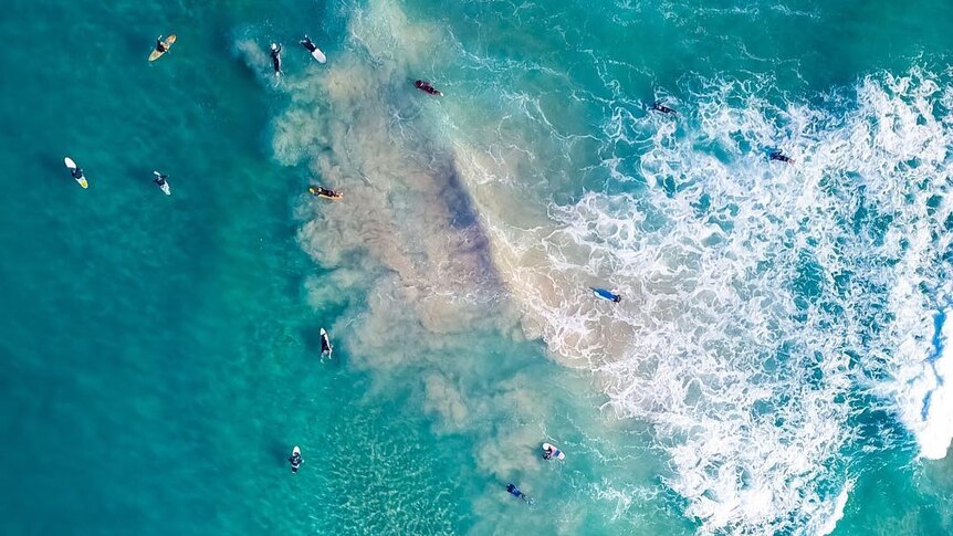 A drone photo of lots of surfers in the water.