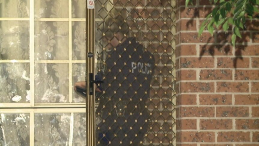 A police officer stands behind a screen door of suburban home.