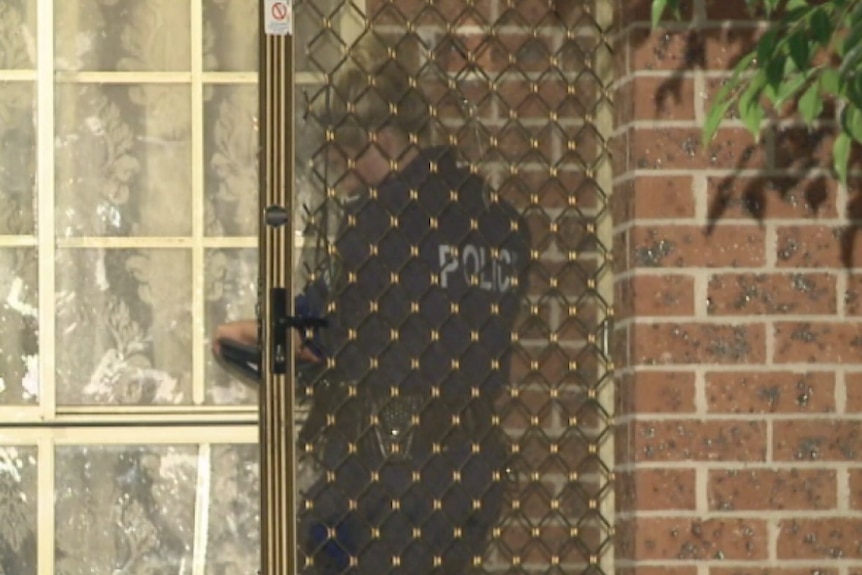 A police officer stands behind a screen door of suburban home.