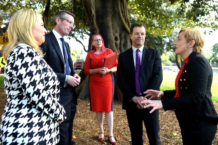 A group of well-dressed people stand under a tree talking. 