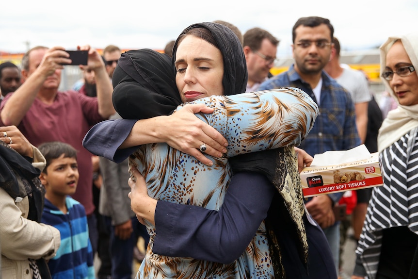 Jacinda Ardern, wearing a black hijab, closes her eyes as she embraces a woman in a full hug