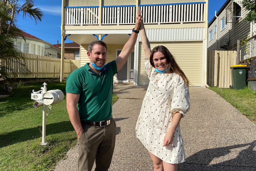 Nikki and Stuart with hands in the air at the driveway of their new home.