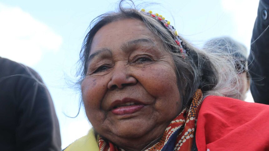 Tight shot of a woman wrapped in an Aboriginal flag looking at the camera.