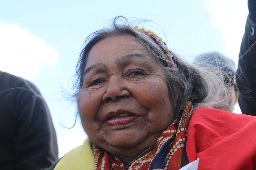 Tight shot of a woman wrapped in an Aboriginal flag looking at the camera.