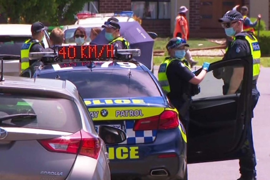 Two police officers stand by their cars at the scene of a murder.