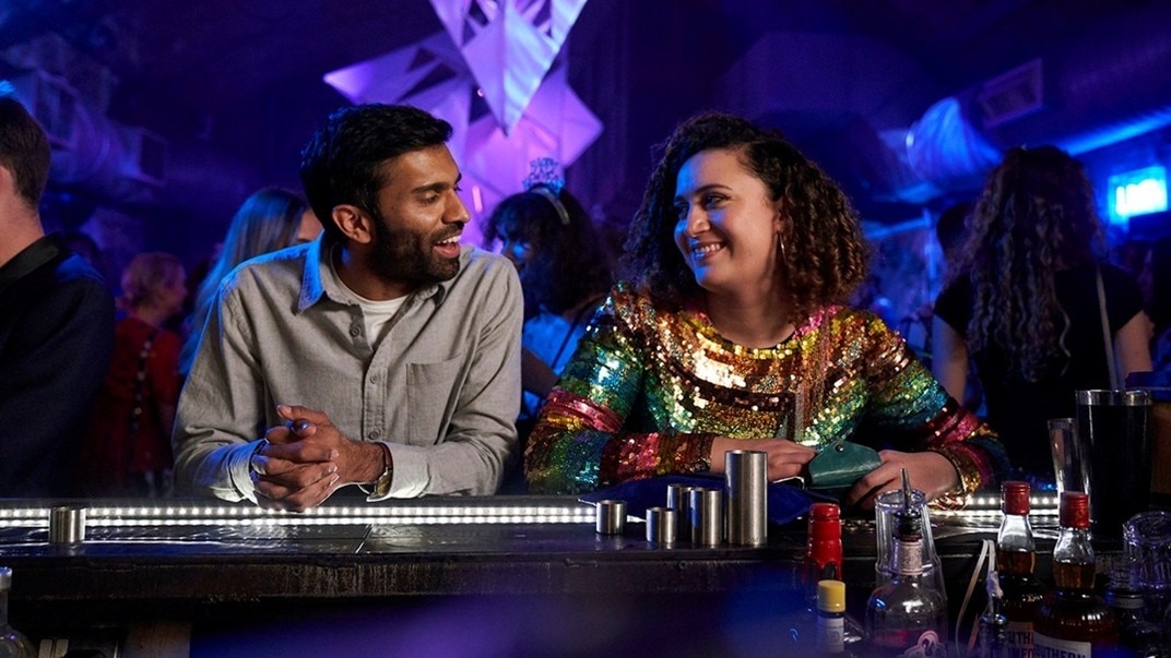 A man and a woman in a bar, both smiling and looking at each other with mutual attraction. 