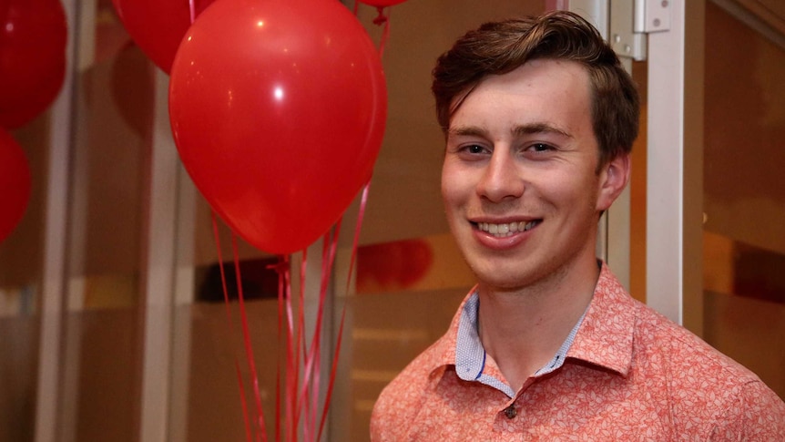 Brighton Labor candidate Declan Martin smiles at the camera in front on red balloons.