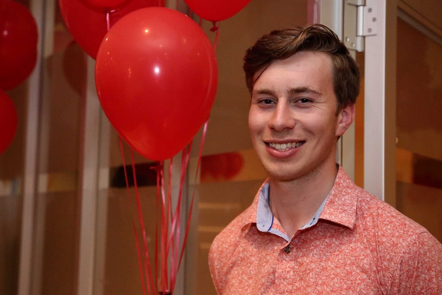 Brighton Labor candidate Declan Martin smiles at the camera in front on red balloons.