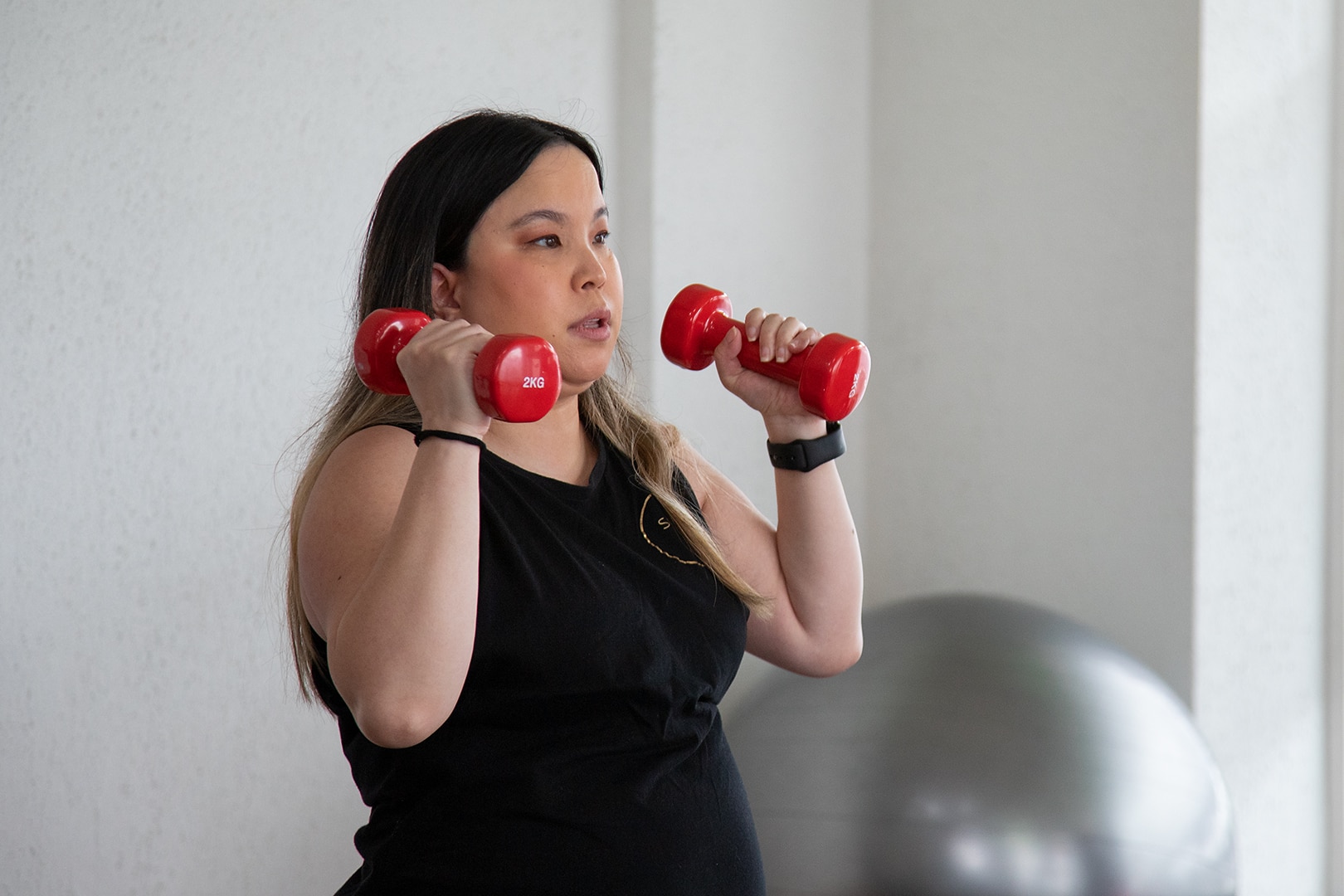 An Asian woman wearing a black singlet is holding red hand weights as she prepares to lift them.