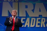 Donald Trump stands in front of a NRA banner about to clap his hands