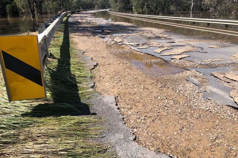 A road pavement on a bridge that has been significantly damaged by rain and flooding