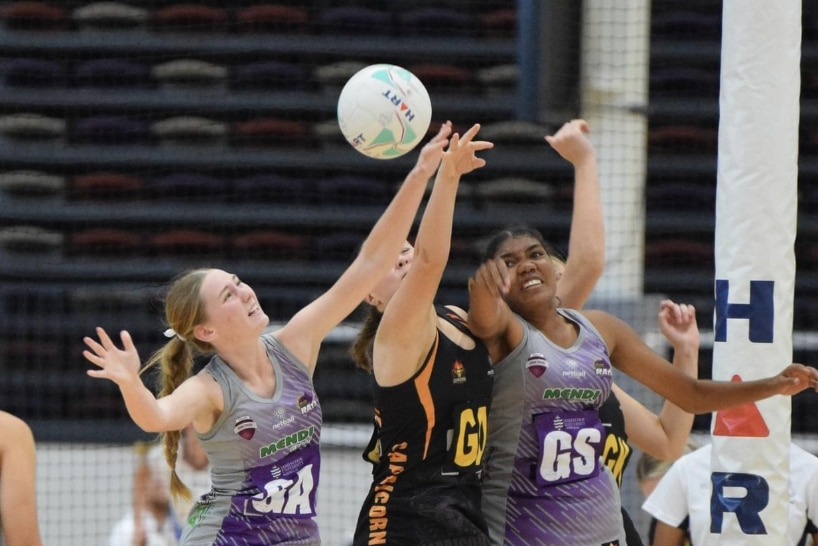 Three young netballers jump in the air trying to get possession of the ball.