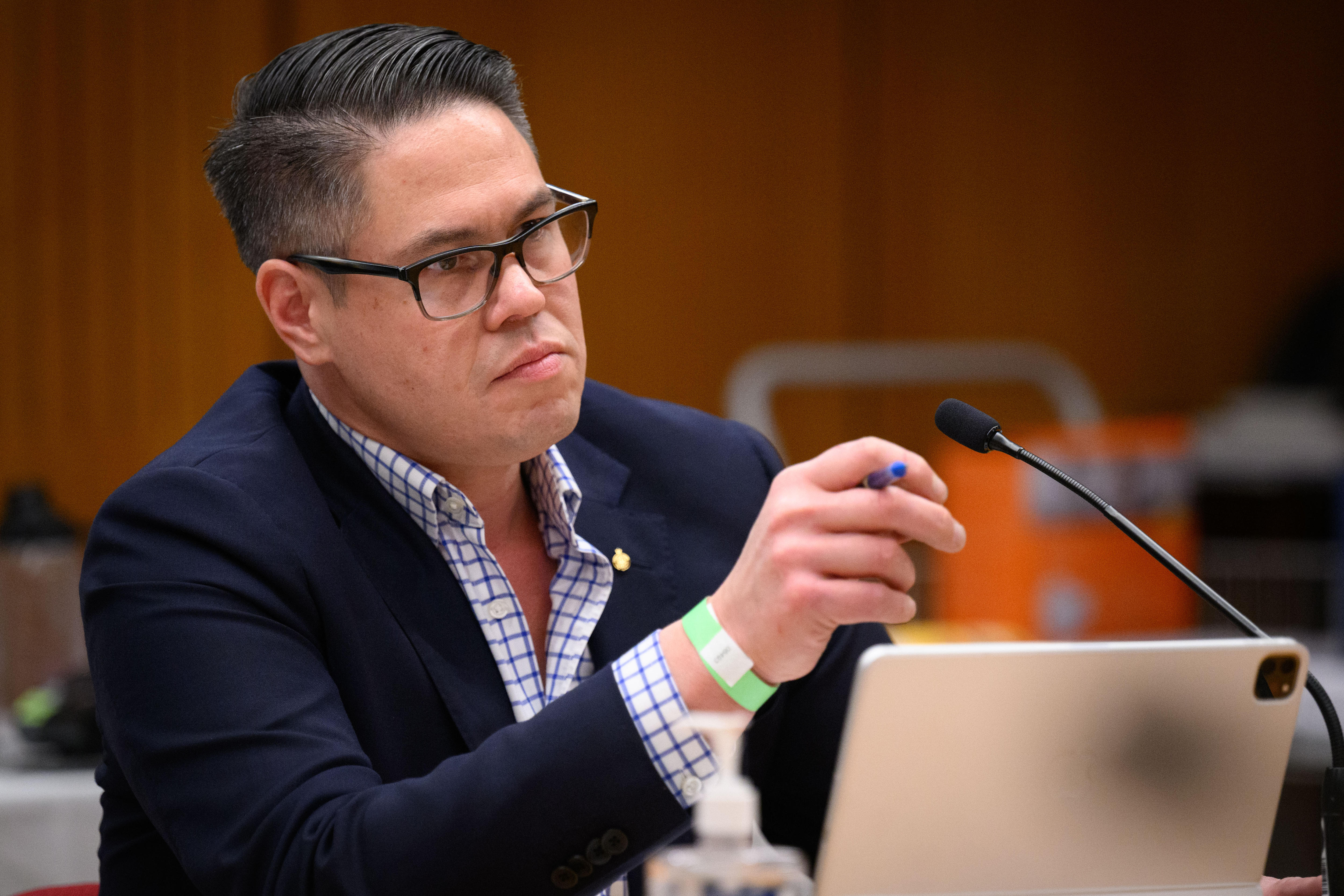 A man wearing glasses and dressed in a suit speaks into a microphone.